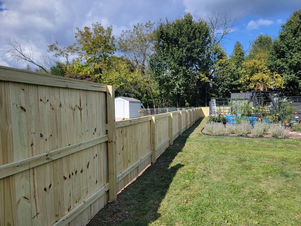 Wooden fence along a grassy yard, under a partly cloudy sky.