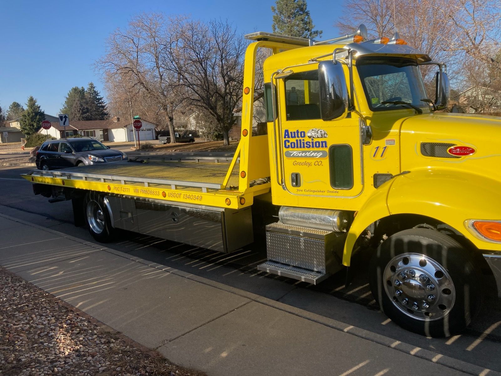 Yellow tow truck parked on a residential street. The flatbed is empty.