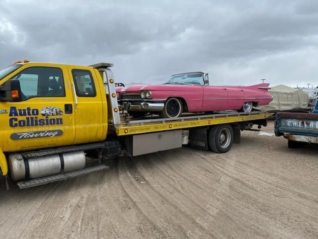 A pink classic convertible is towed on a yellow tow truck with the words "Auto Collision Towing" on the side.