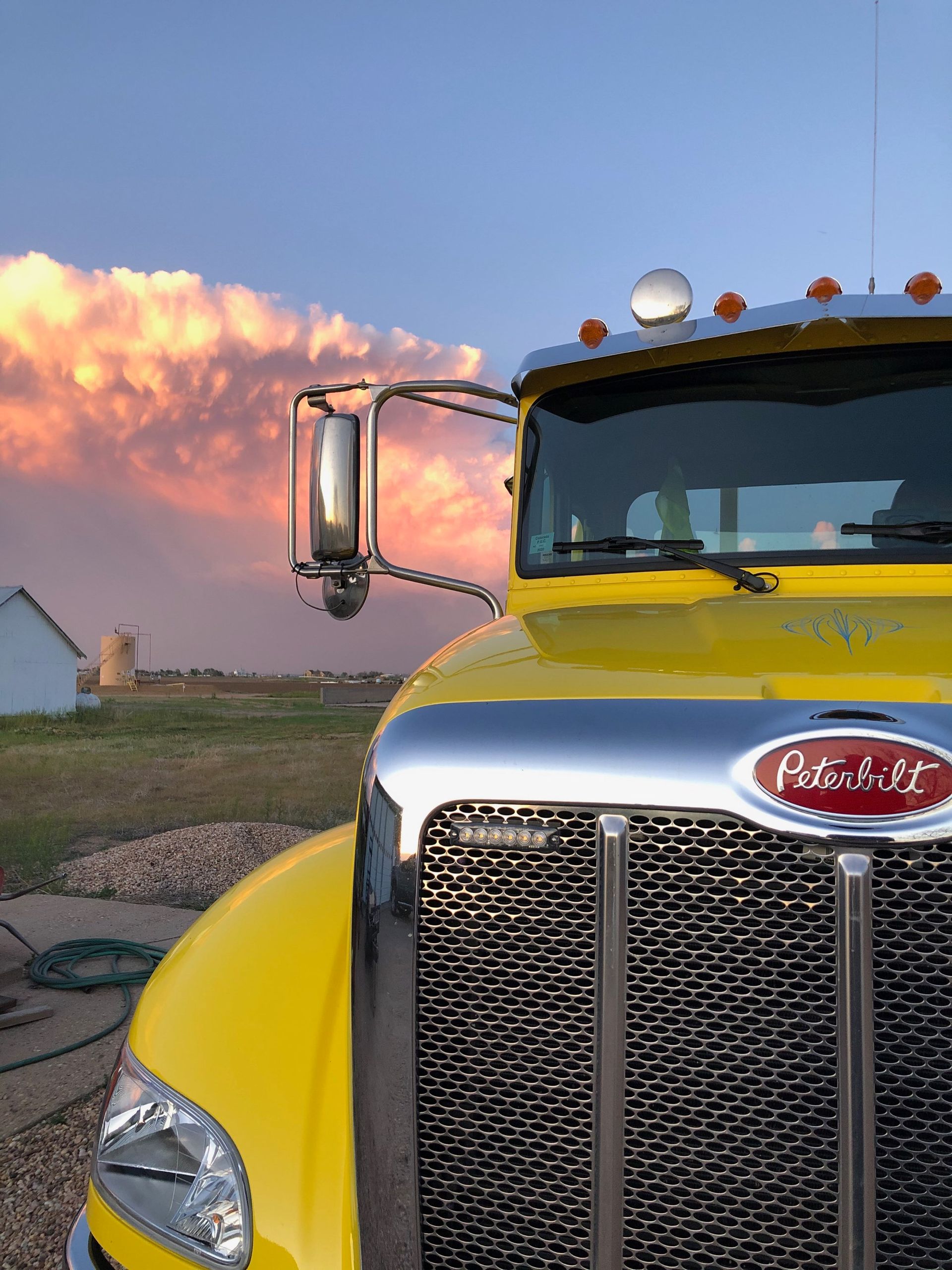Yellow Peterbilt semi-truck parked in front of a rural landscape with colorful sunset.