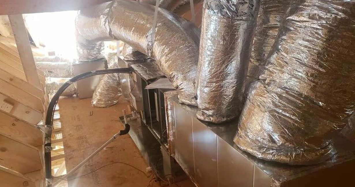 HVAC ductwork in an attic, wrapped in silver insulation, connected to a unit.