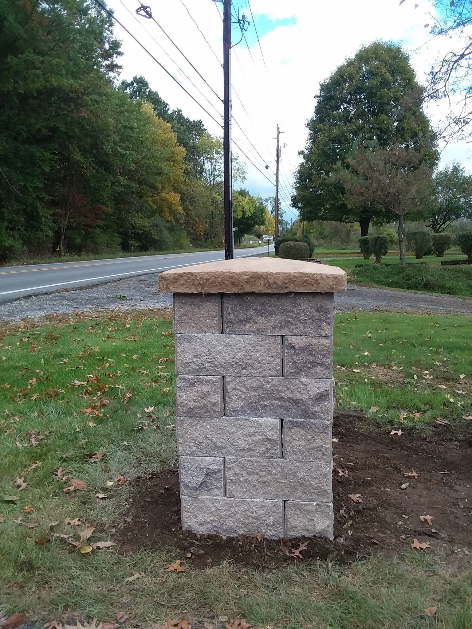 Brick pillar with a brown cap, pole, and a road in the background.