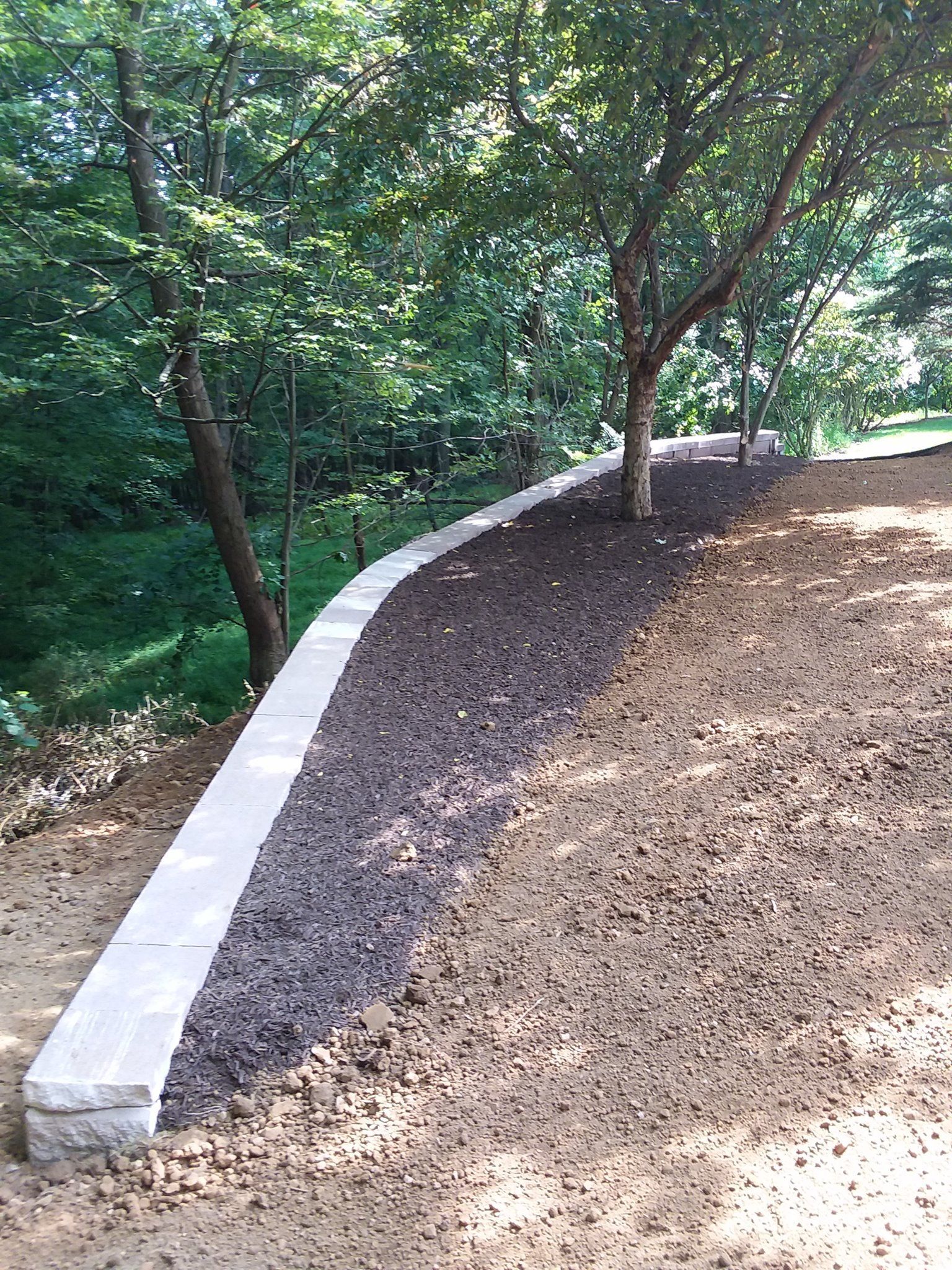 Stone retaining wall along a hillside path, with trees in the background.