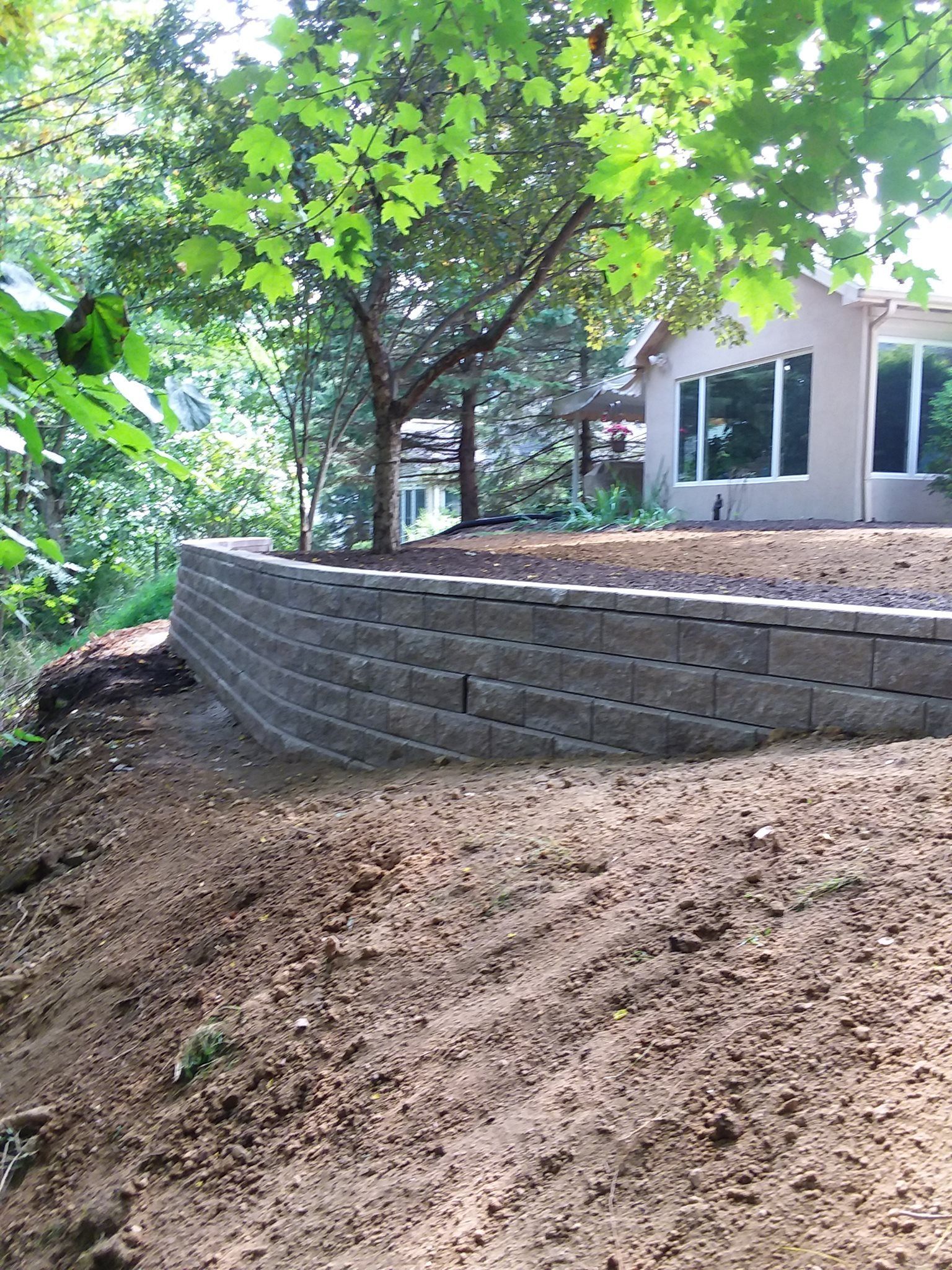 Retaining wall made of gray blocks in a yard, under a tree, with a house in the background.