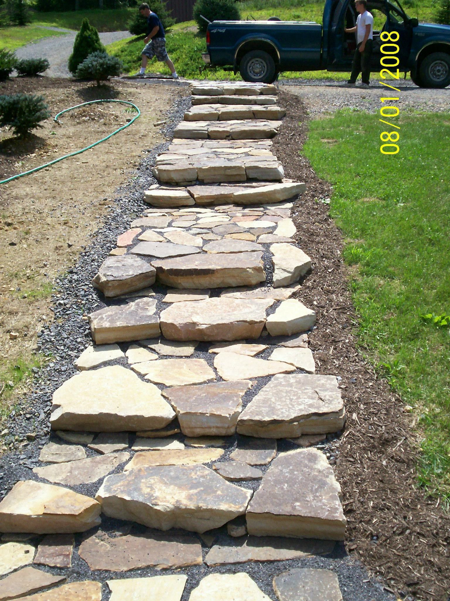 Stone steps leading through a yard; two people near a truck, a person working in the background.