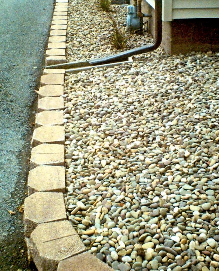 Stone brick edging along a driveway and gravel bed near a building.