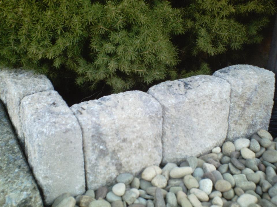 Stone border edging a rock garden with green foliage in the background.