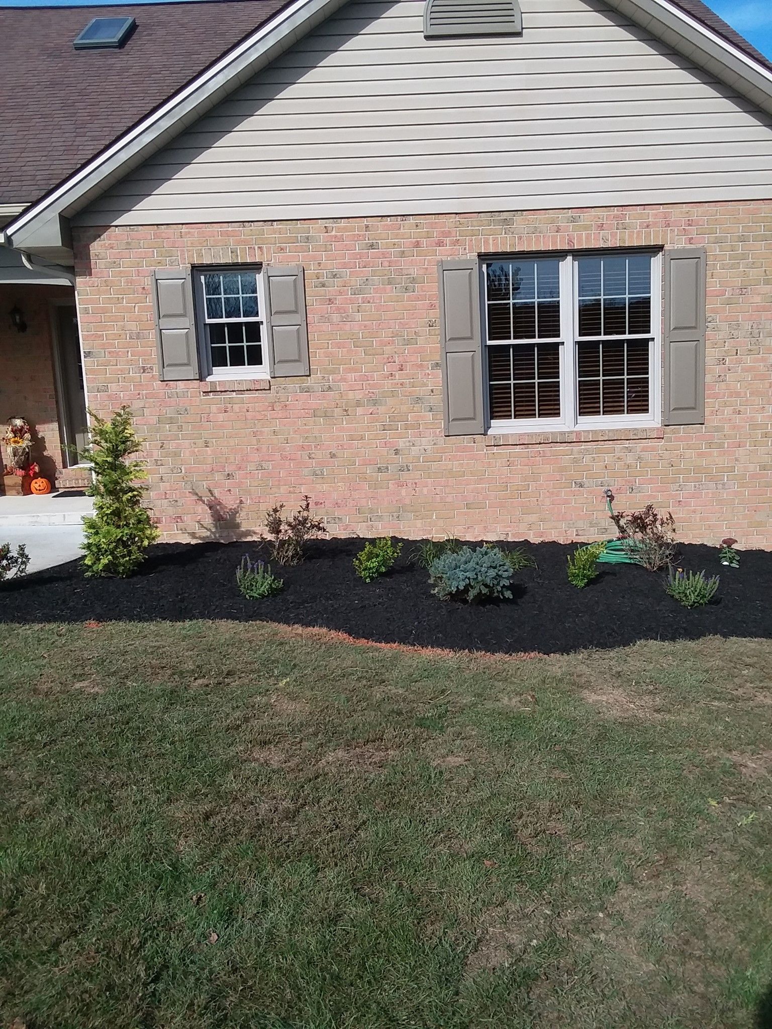 Brick house exterior with brown shutters and new landscaping with black mulch.