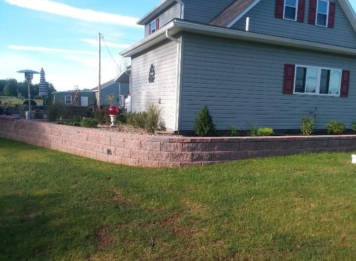 House with a brick retaining wall and lawn. Blue siding, red shutters, and blue sky.