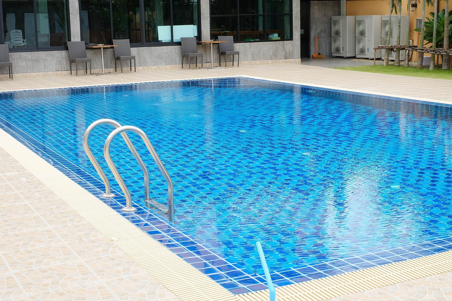 Outdoor swimming pool with blue water and metal ladder beside lounge chairs and tables