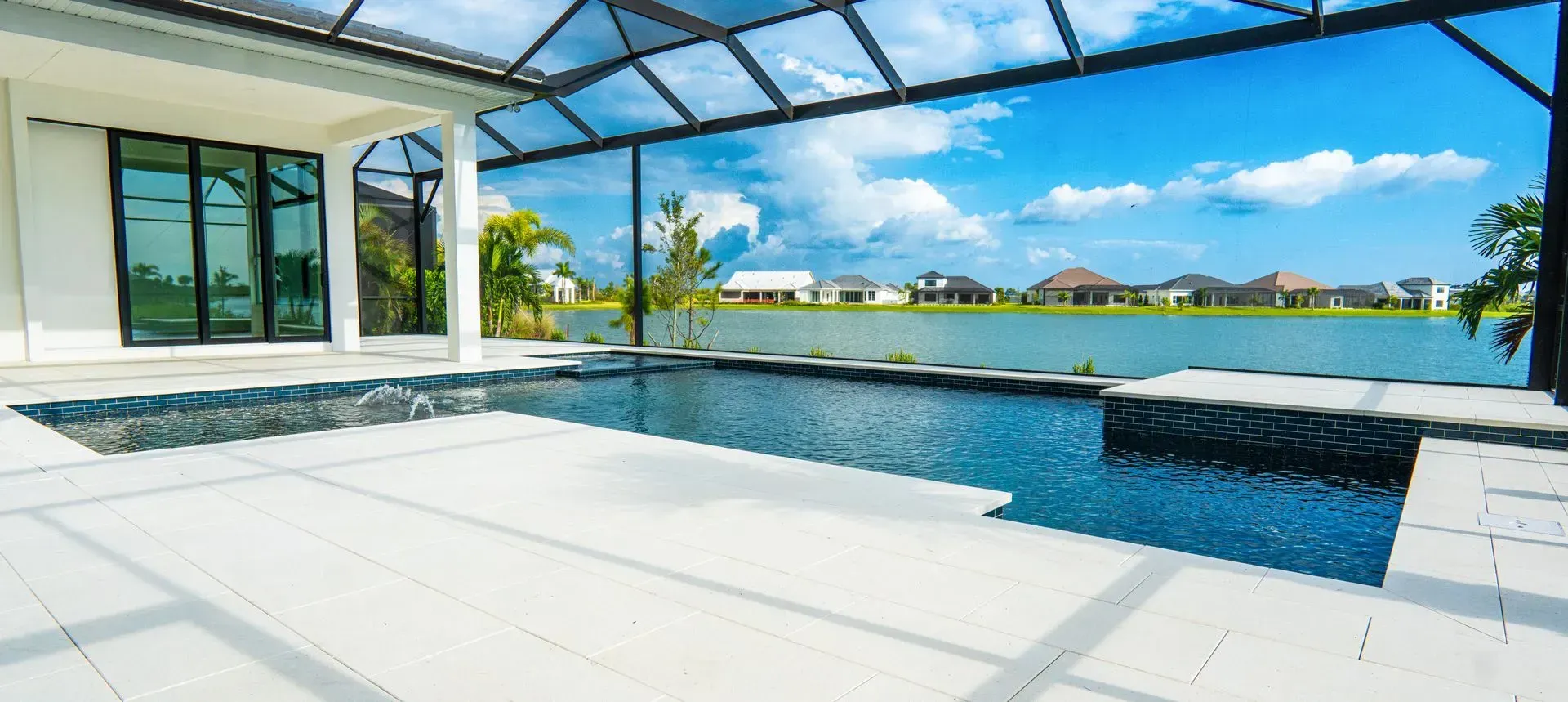 Modern patio with infinity pool, glass canopy, and waterfront view under a blue sky