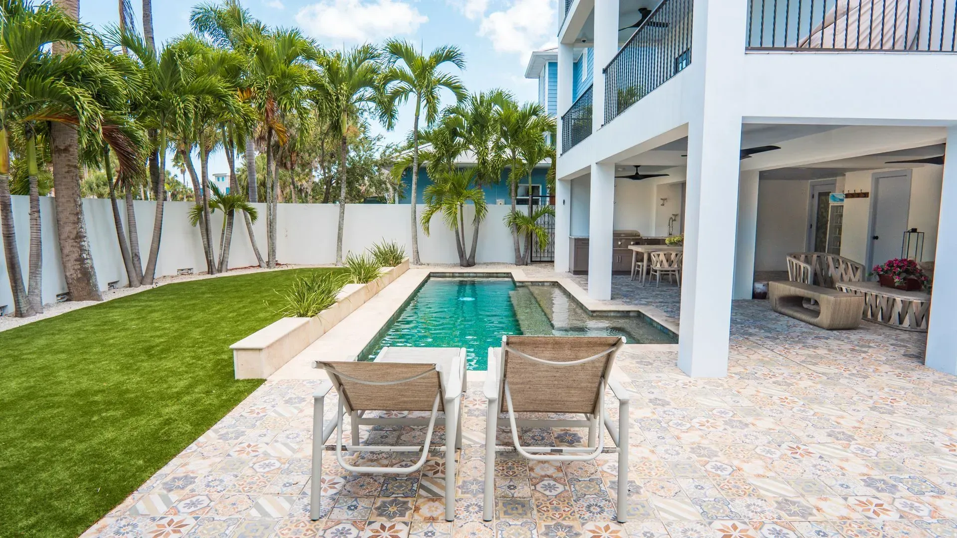 Modern patio with pool, lounge chairs, palm trees, and a covered outdoor seating area.