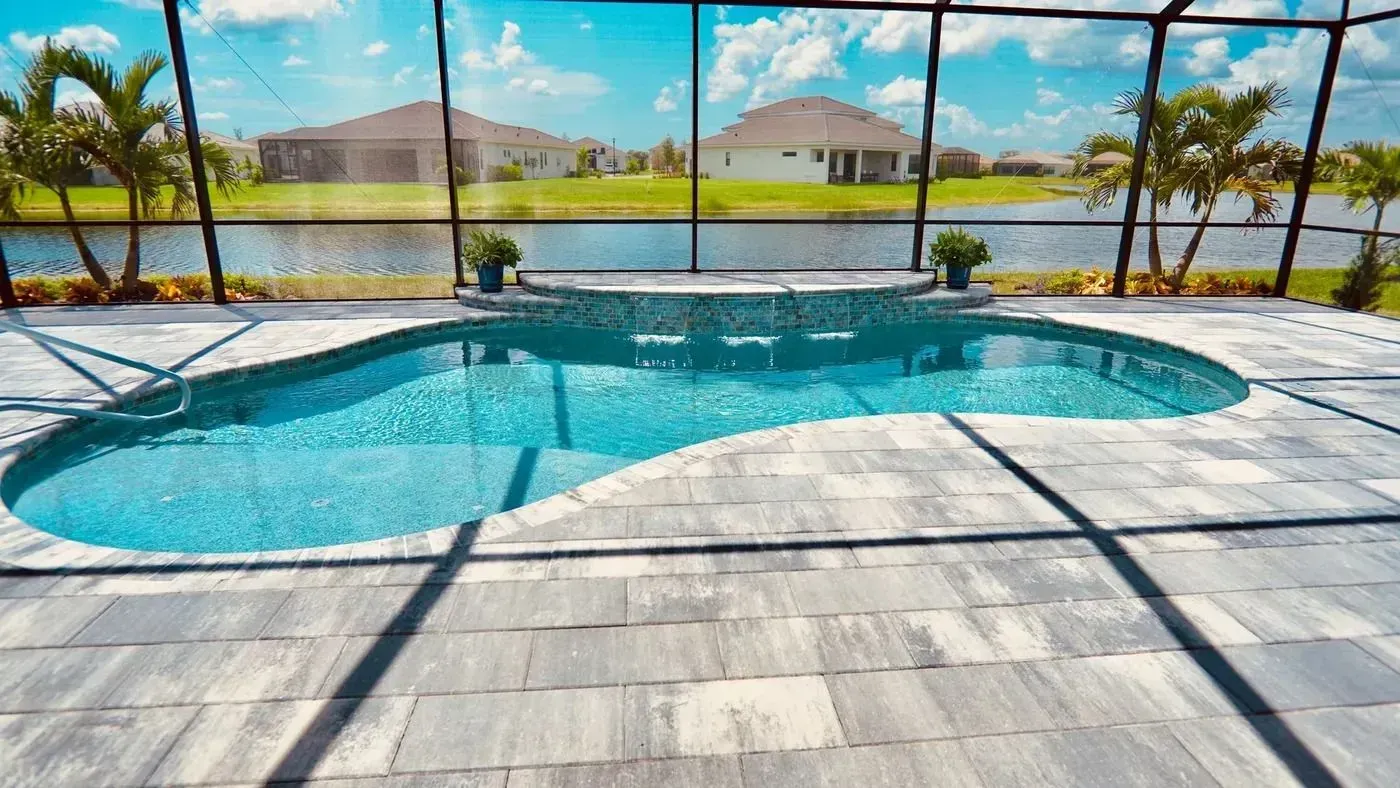 Backyard pool with turquoise water, screened enclosure, and lake view beyond the patio.