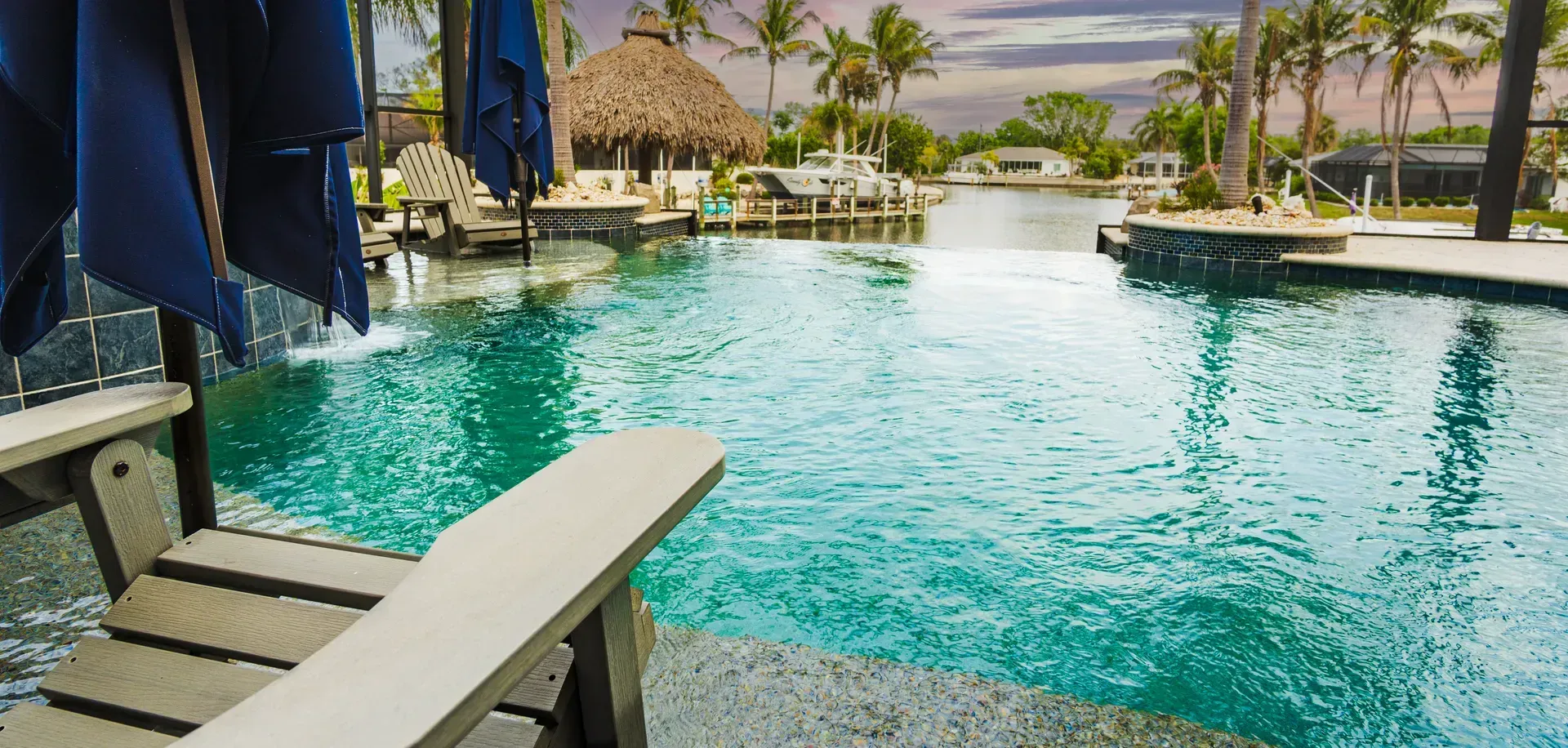 Tropical resort pool with turquoise water, lounge chairs, palm trees, and thatched-roof huts