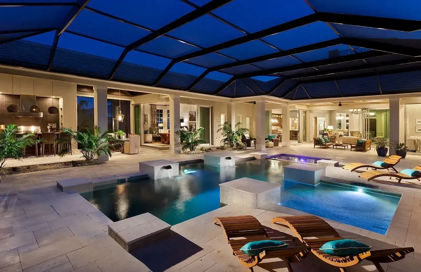 Luxury indoor-outdoor pool with blue lighting, lounge chairs, and a covered patio at night