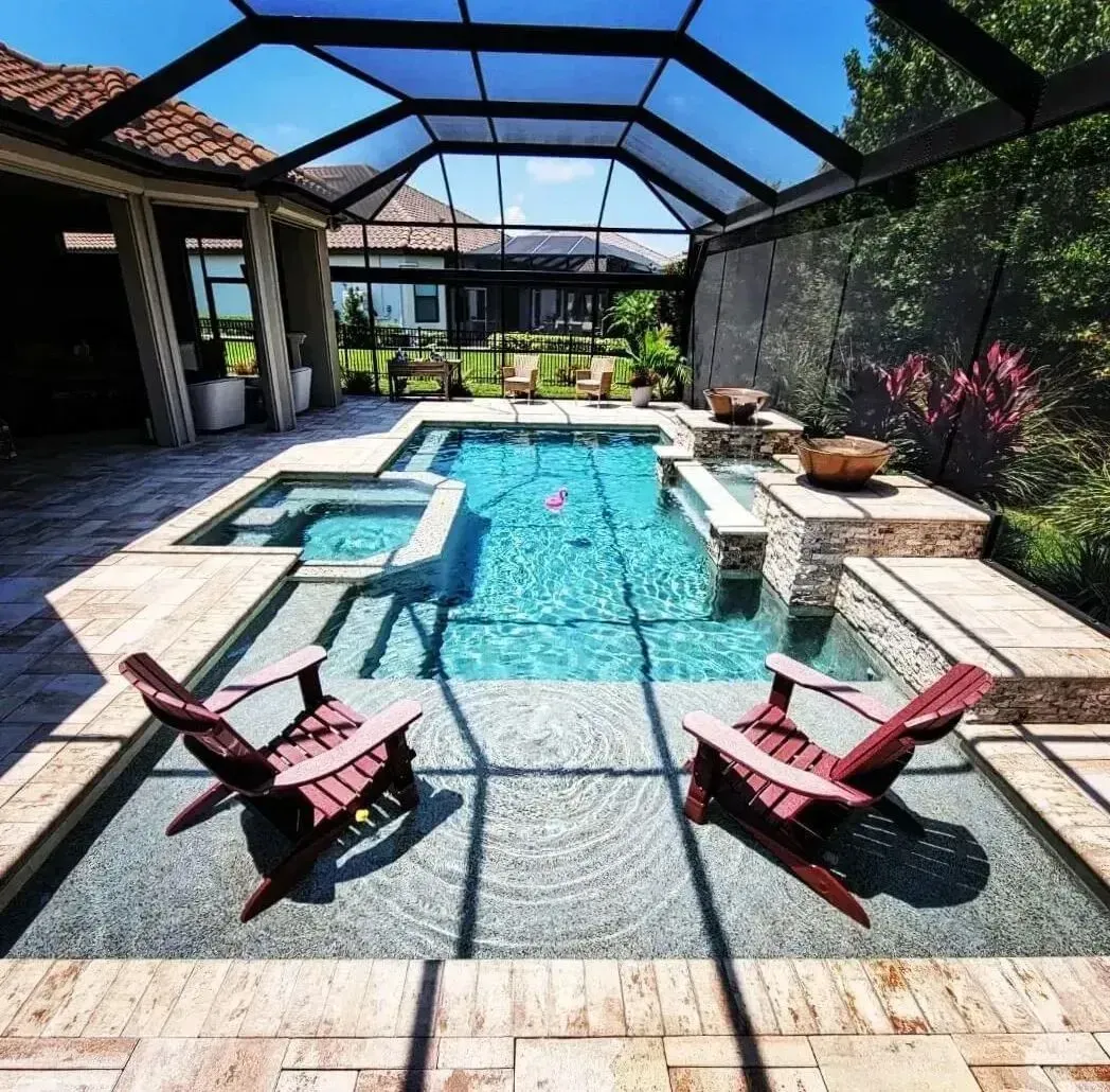 Modern backyard pool with blue water, stone patio, and two red lounge chairs under a screened enclosure