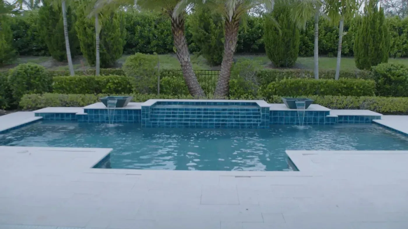 Backyard swimming pool with blue water, white patio, and tropical landscaping