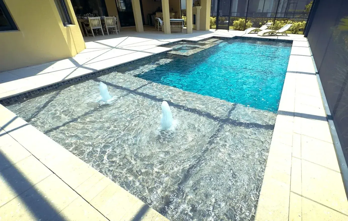 Sunny outdoor swimming pool with clear blue water and tiled deck, shaded by nearby building columns