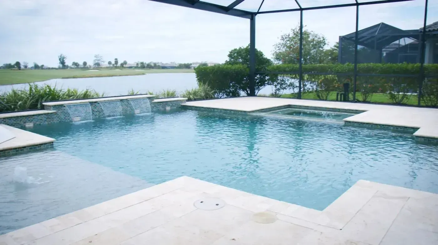 Infinity pool beside a lake, with blue water, white stone deck, and green landscape beyond.