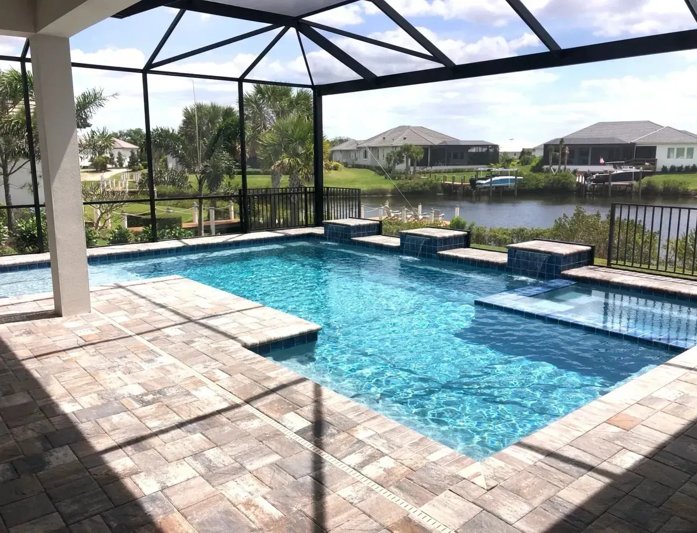 Covered backyard pool with blue water, stone patio, and water views under a screened enclosure