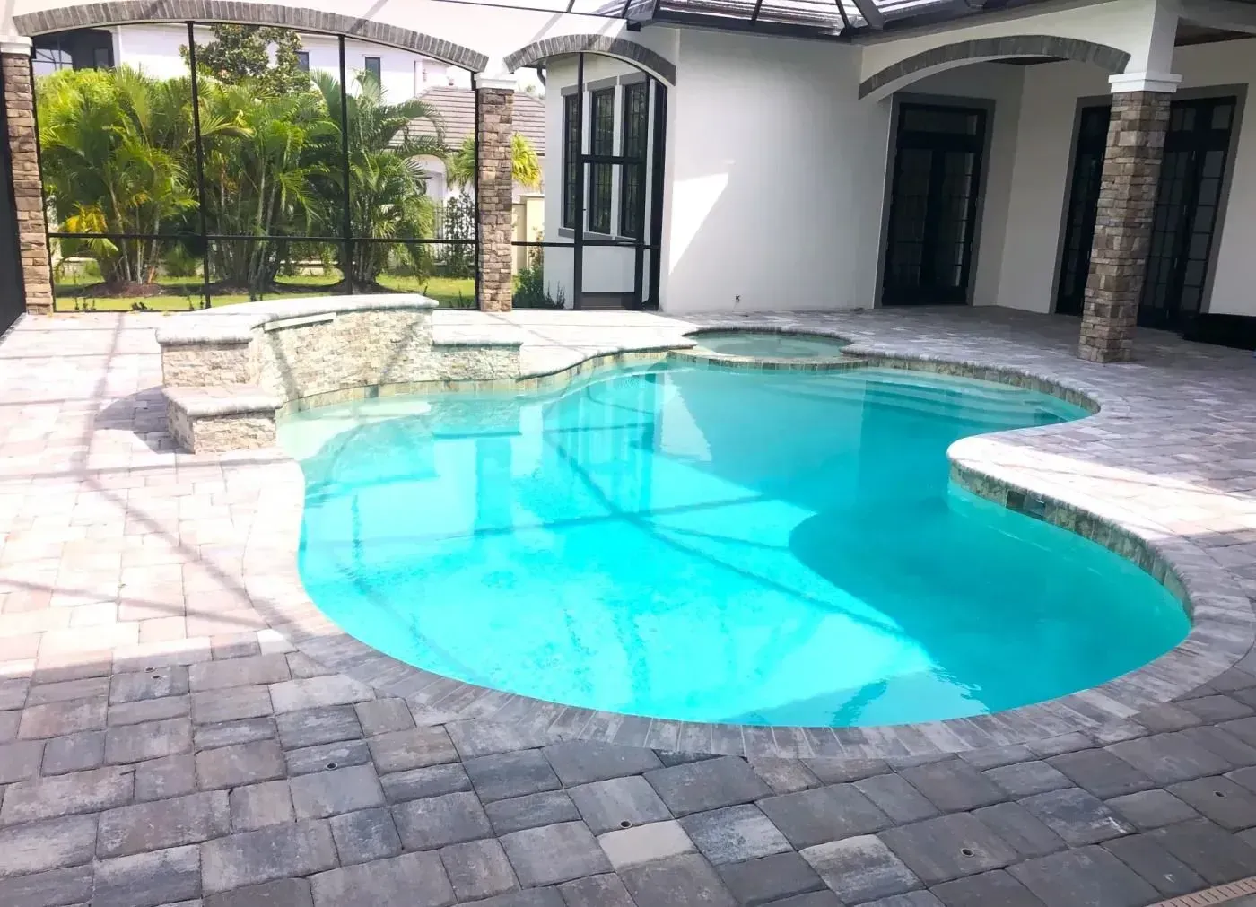 Backyard pool with clear blue water, stone patio, and white house exterior