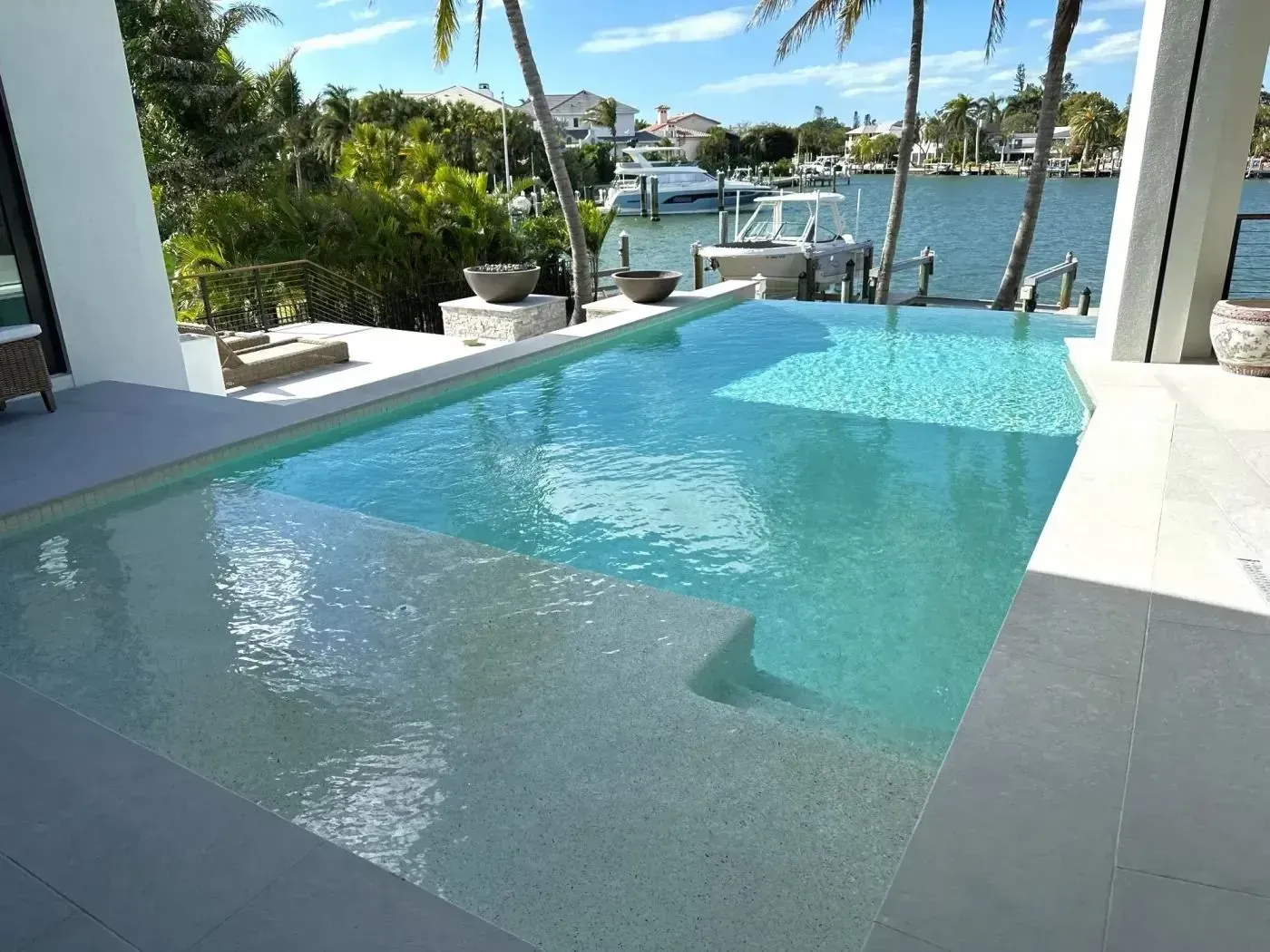 Infinity pool overlooking a marina with palm trees and bright blue water