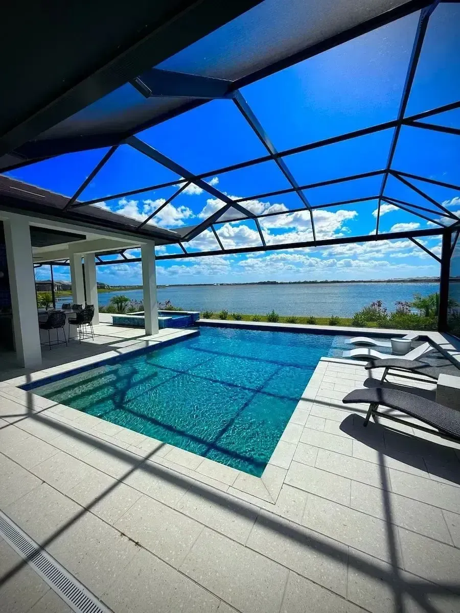 Covered patio with blue pool, lounge chairs, and ocean view under a bright sky