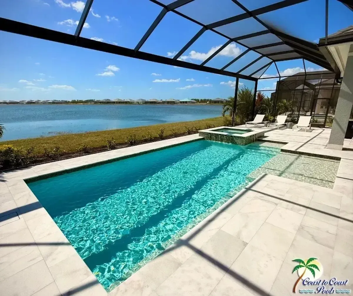 A turquoise pool beside a waterfront patio, with white lounge chairs and a screened canopy under a blue sky.