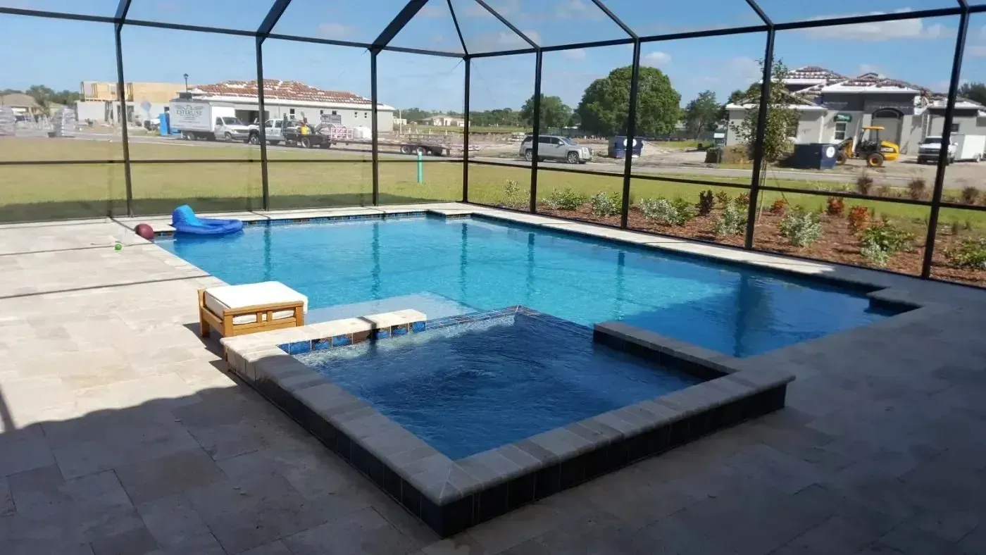 Screen-enclosed backyard pool with blue water, hot tub, and patio seating under a clear sky