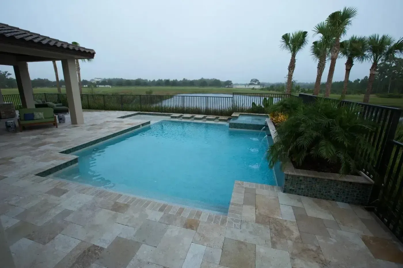 Patio with a swimming pool overlooking a calm waterfront and palm trees at dusk