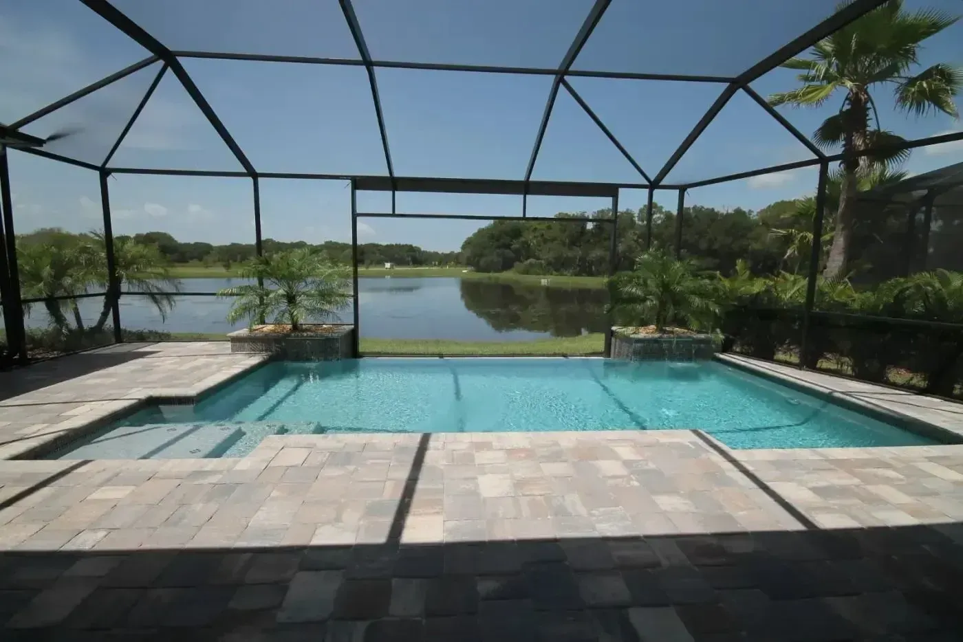 Screened backyard pool with stone deck and lake view under a metal enclosure