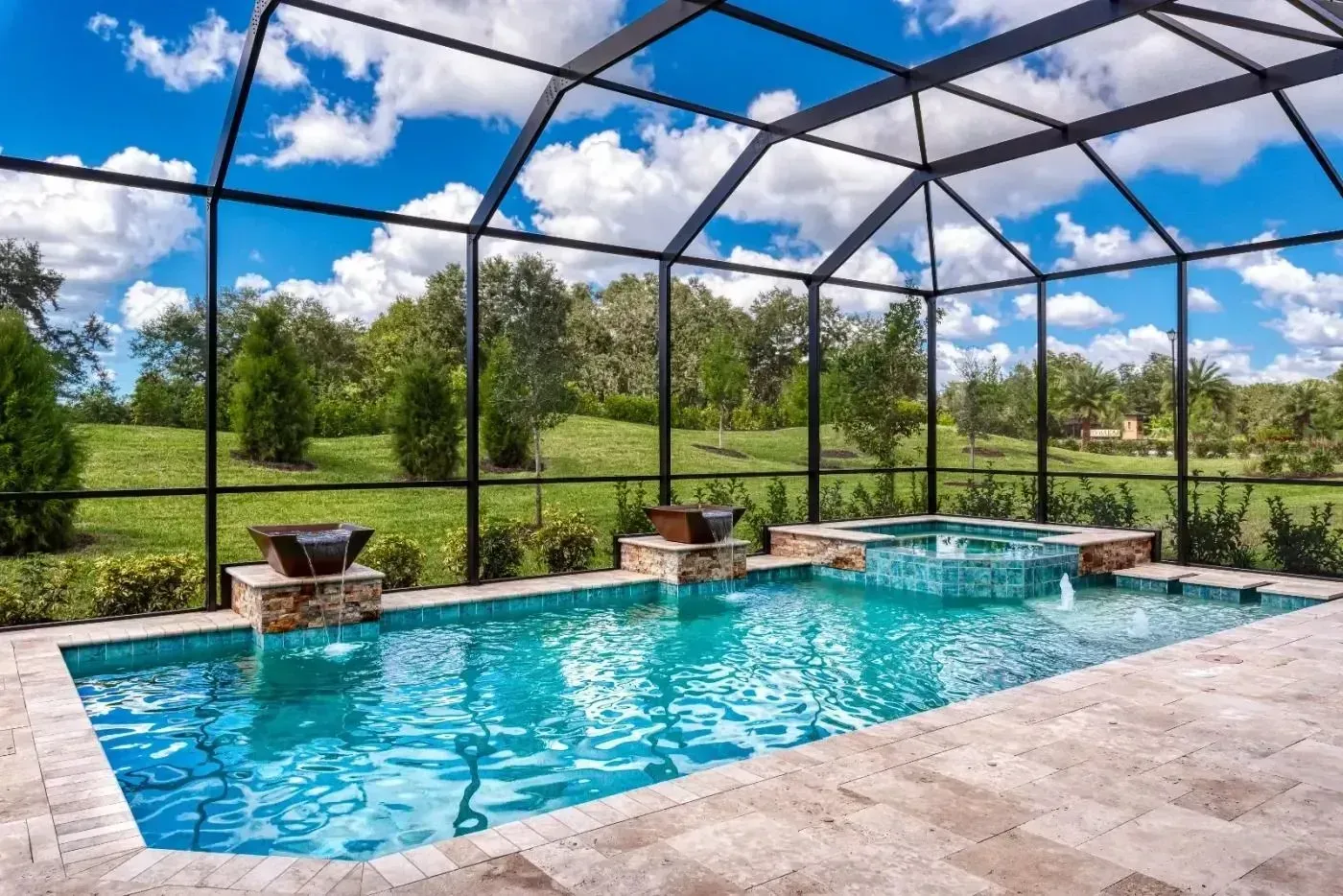 Screened backyard pool with blue water, stone patio, and lush green lawn under a partly cloudy sky