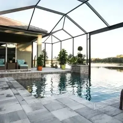 Modern patio with a screened-in pool and covered deck overlooking water at sunset