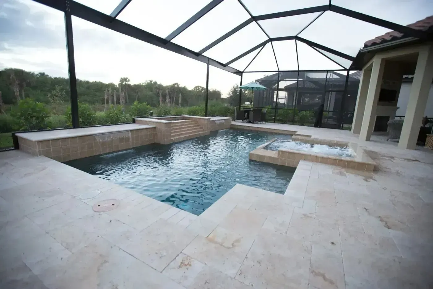 Modern backyard pool with stone patio and screened enclosure, overlooking greenery