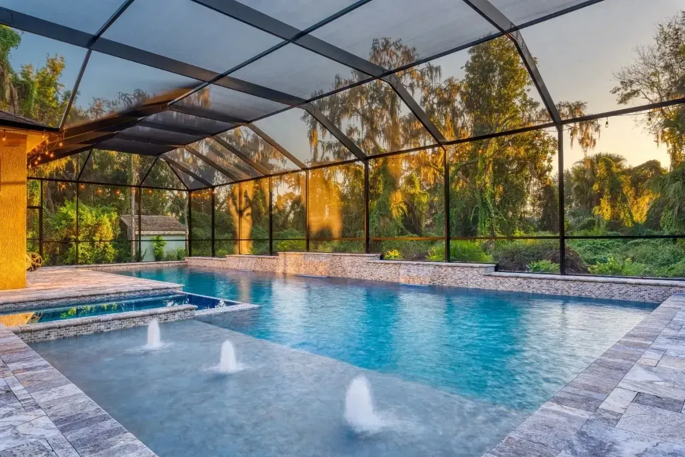 Screened-in backyard pool with fountains and sunset-lit trees beyond the enclosure