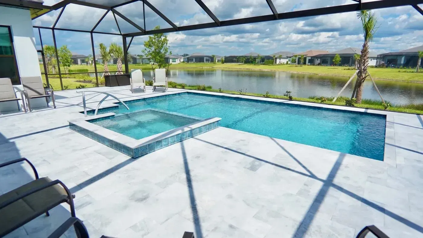 Screened-in patio with a blue pool, lounge chairs, and a lake view under a sunny sky