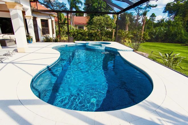 Curved blue swimming pool beside a white patio and green lawn in a sunny backyard