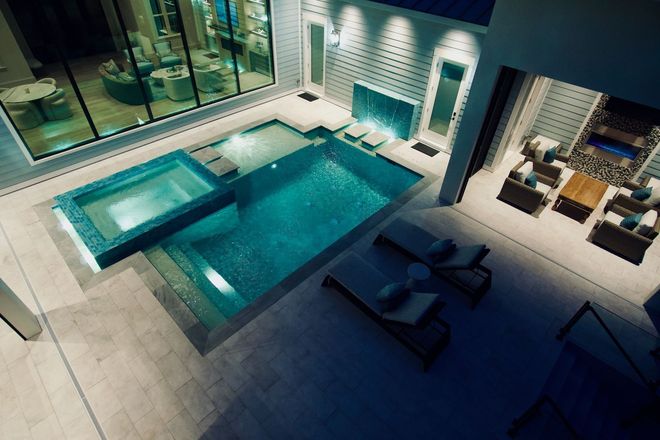 Modern indoor pool courtyard at night with blue water, lounge chairs, and tiled walls