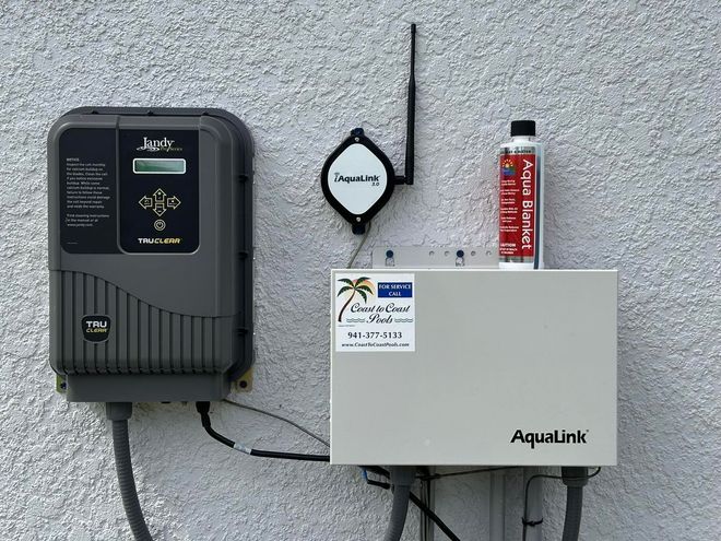 Outdoor utility wall with black meter, gray AquaLink box, antenna, and fire extinguisher mounted on stucco.