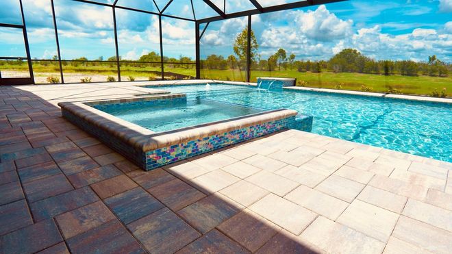 Backyard pool with raised spa, blue water, and paver patio under a screened enclosure
