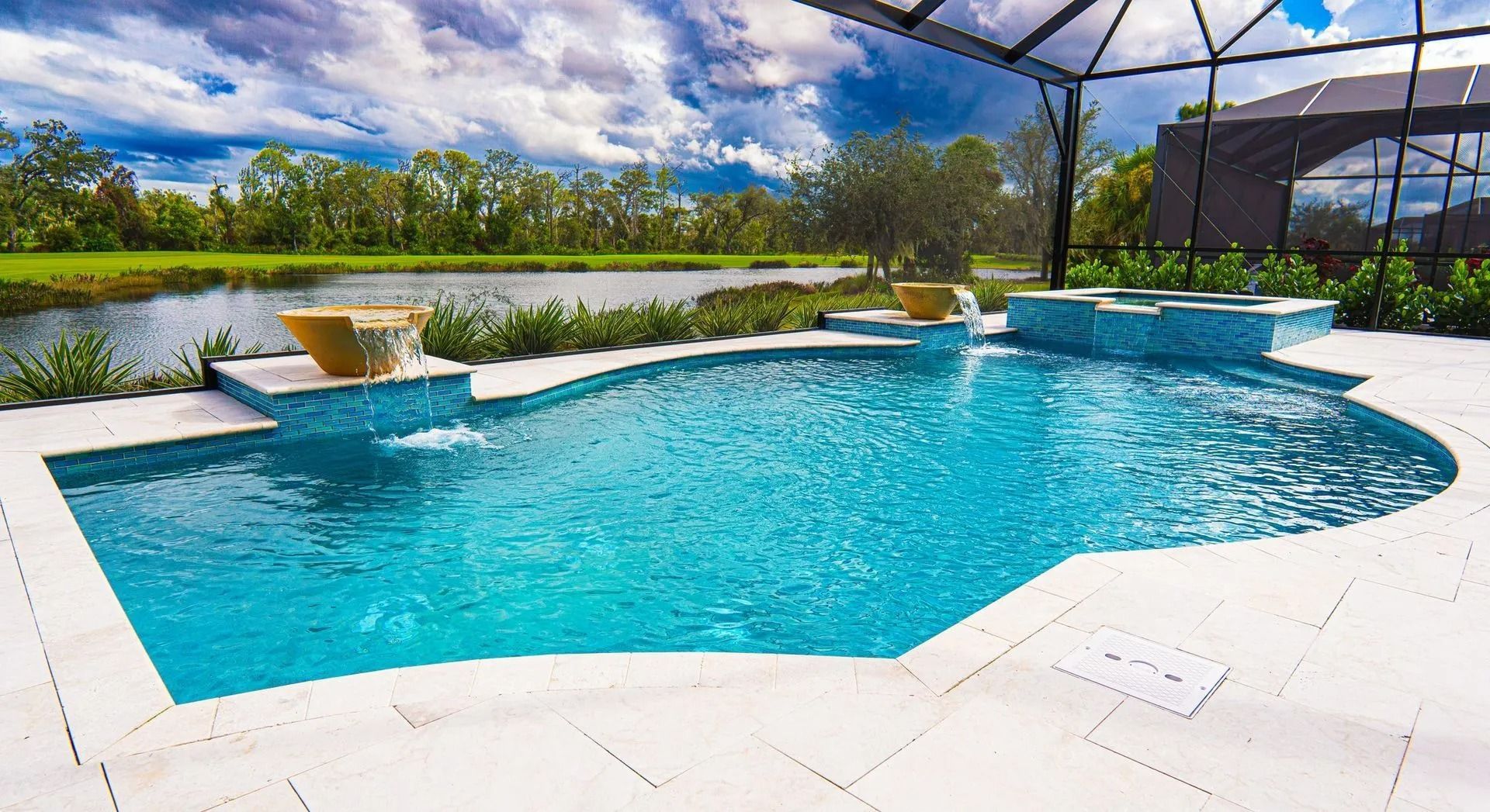 Curved backyard swimming pool with blue water, white patio, and a lake view under a sunny sky