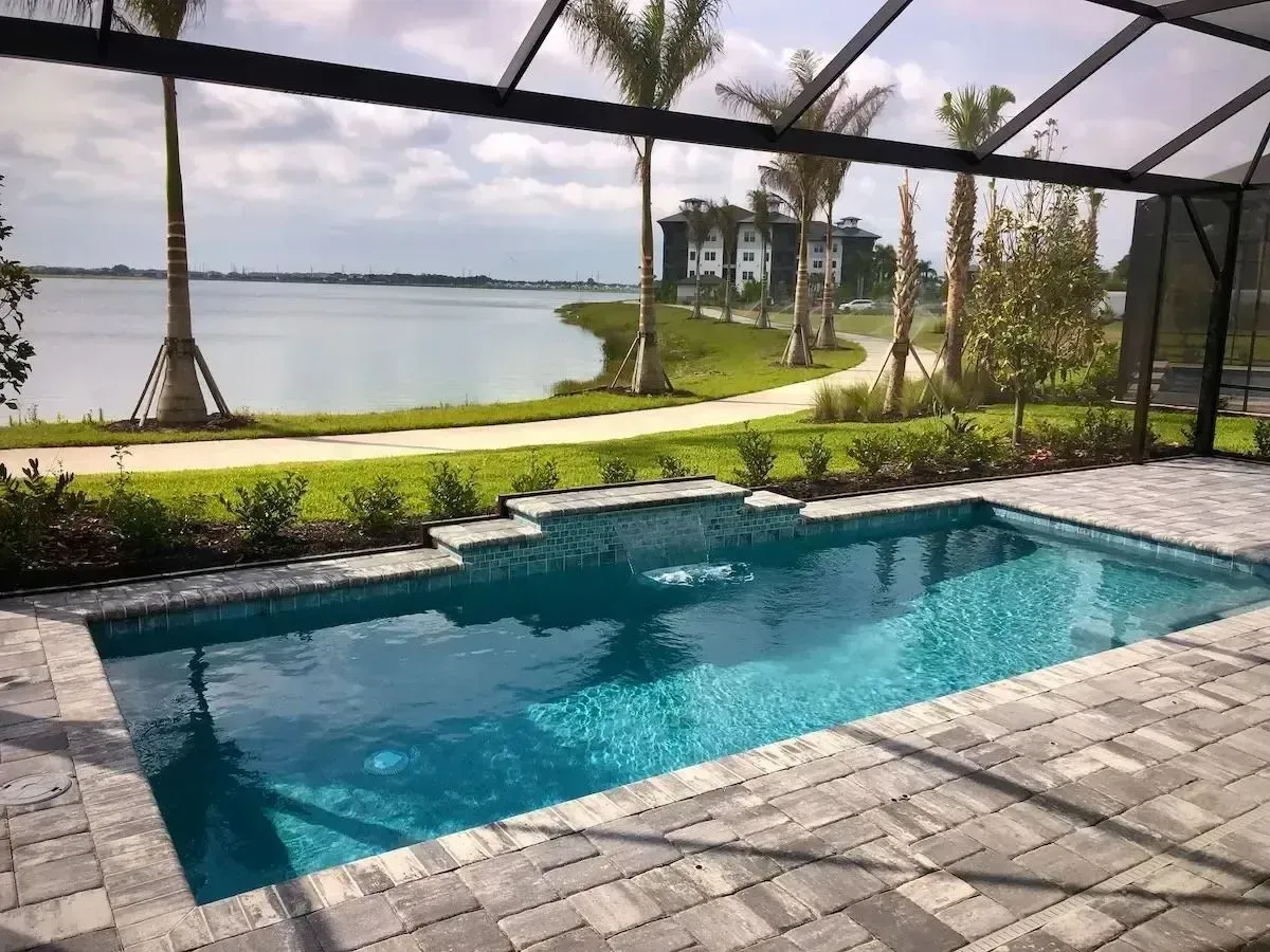 Screened patio with a turquoise pool overlooking a calm lake and landscaped yard