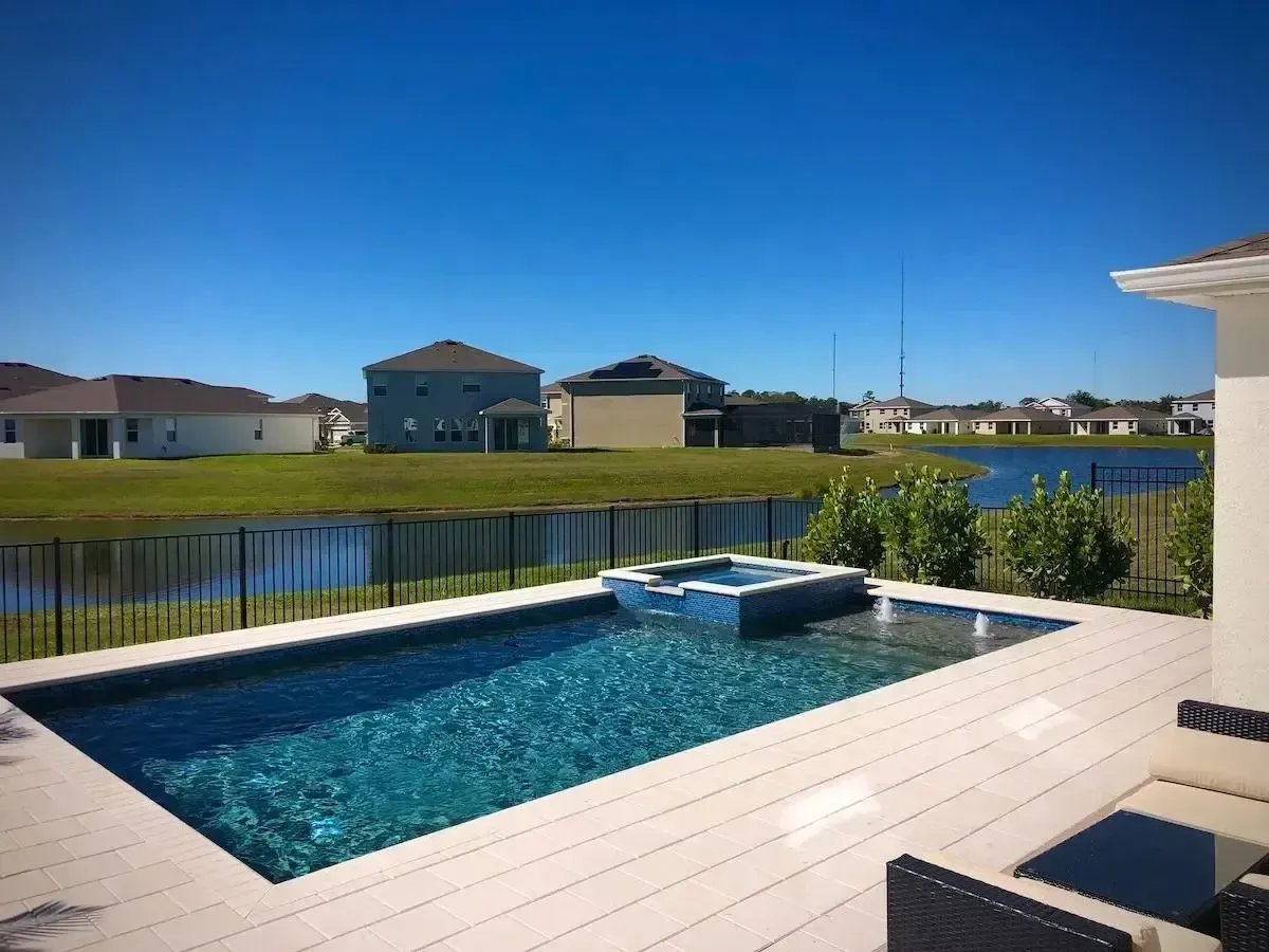Backyard patio with a small blue pool, canal view, and houses under a clear blue sky.