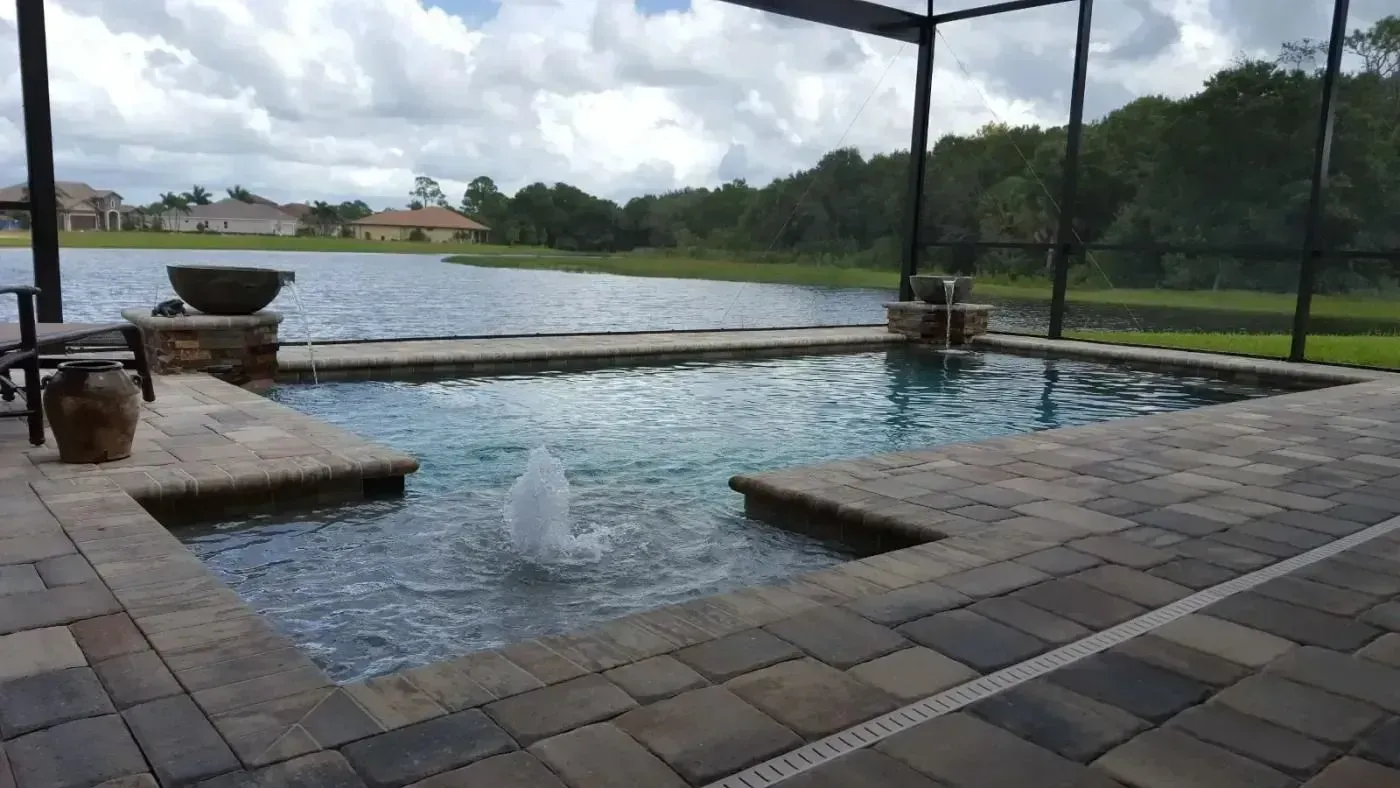 Covered outdoor swimming pool with stone deck, overlooking green landscape under a cloudy sky