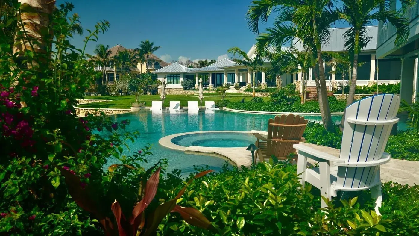 Tropical resort pool with white Adirondack chairs, palm trees, and blue water under a sunny sky