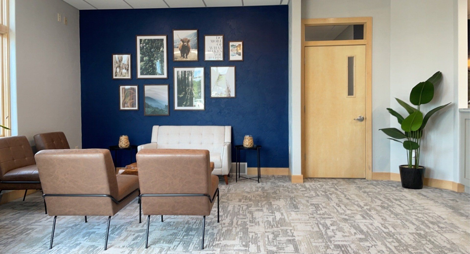 Cozy waiting area with tan chairs, blue accent wall with framed artwork, and a potted plant.