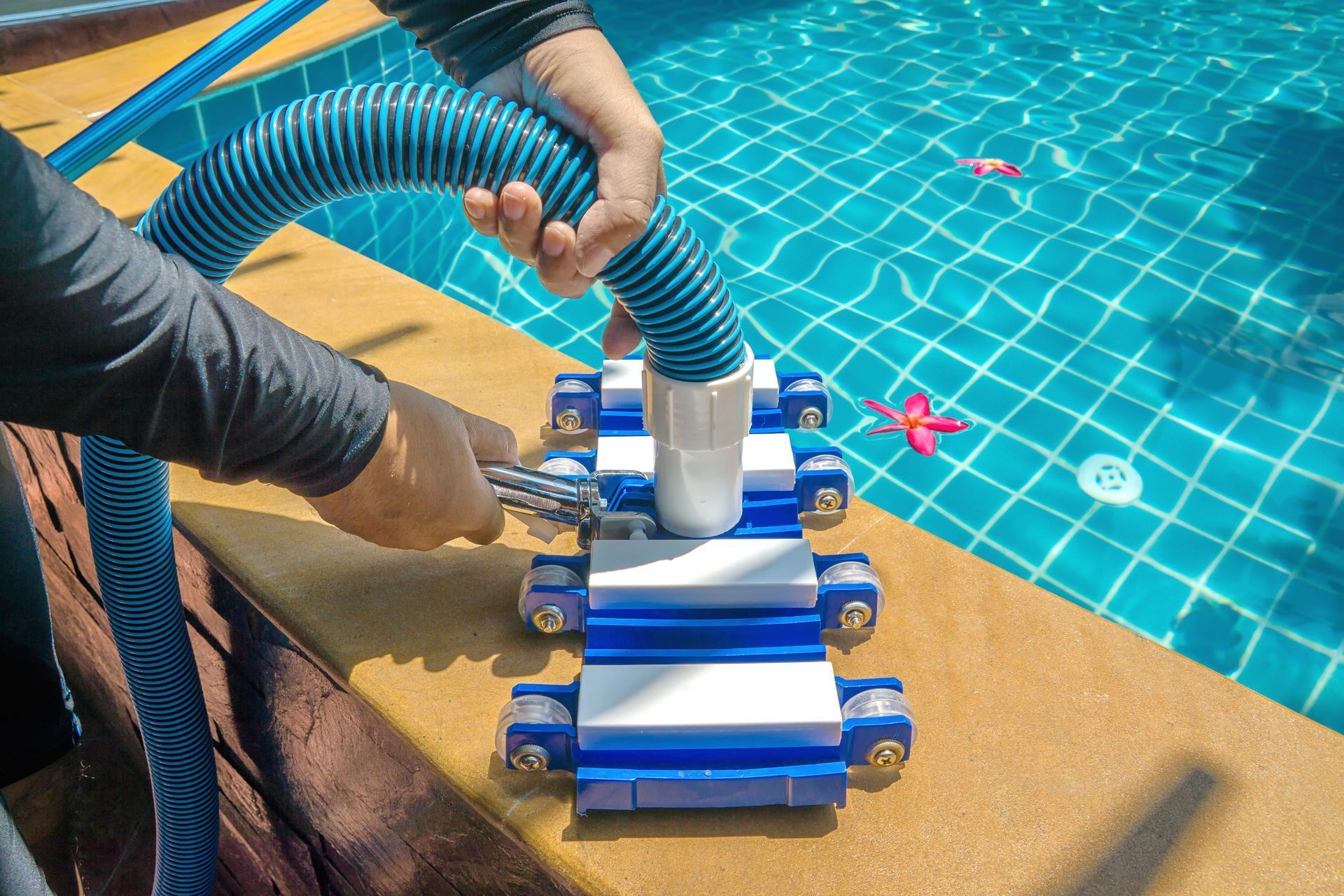 Person uses a pool vacuum cleaner to clean the edge of a blue tiled swimming pool.