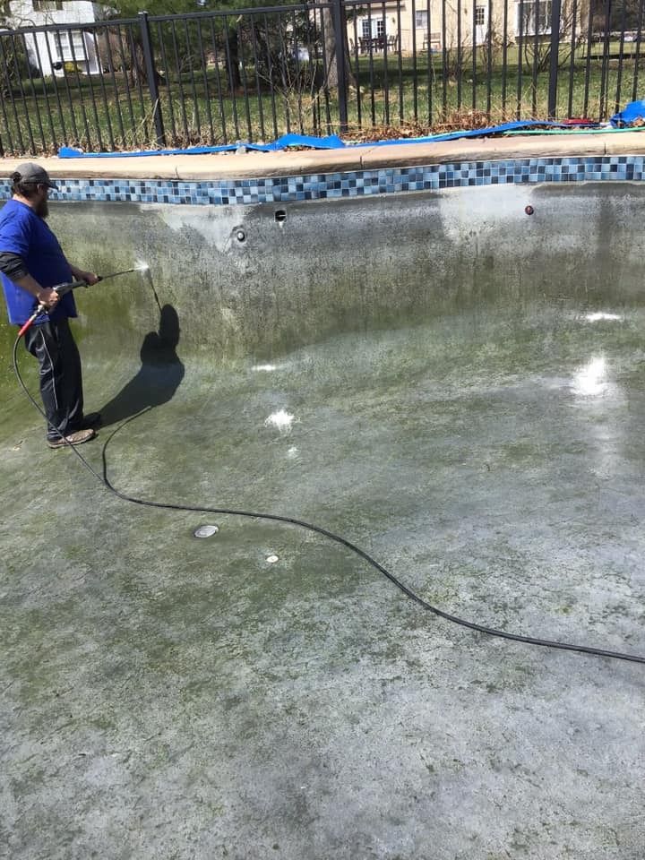 Person spraying algae in an empty, green-stained swimming pool.