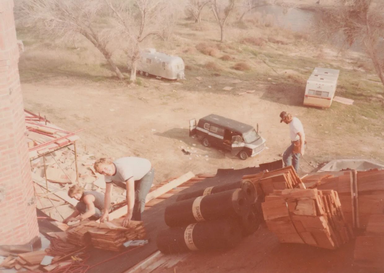 Workers unloading a truck in a dusty yard with a black car and trees in the background.