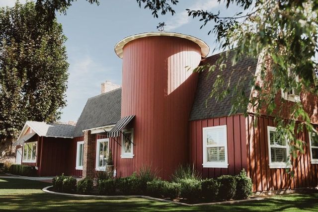 Red farmhouse with a round silo-like tower, white-trimmed windows, and trees in front